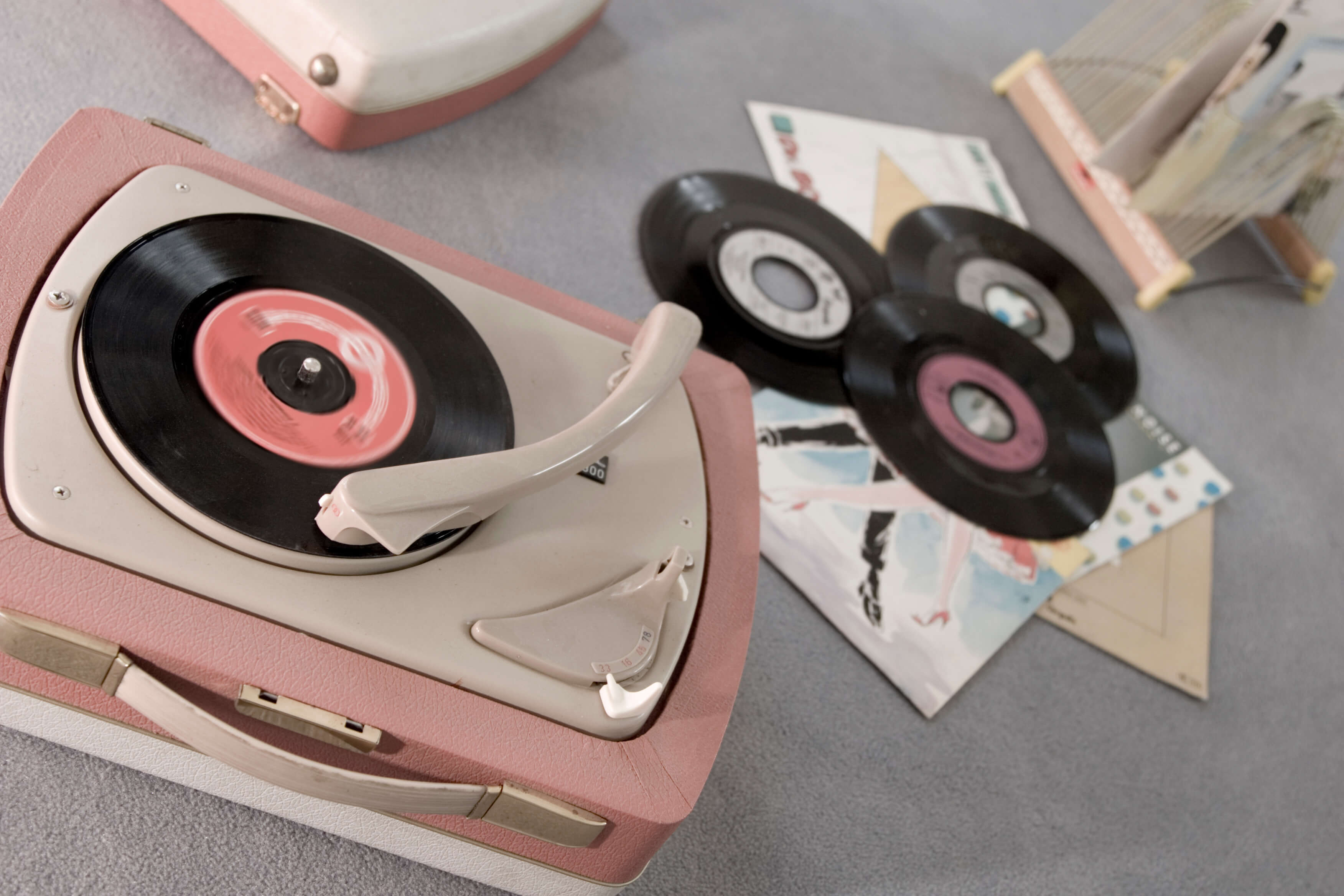 a pink vinyl record player playing a vinyl record with other discs laying next to it on the floor