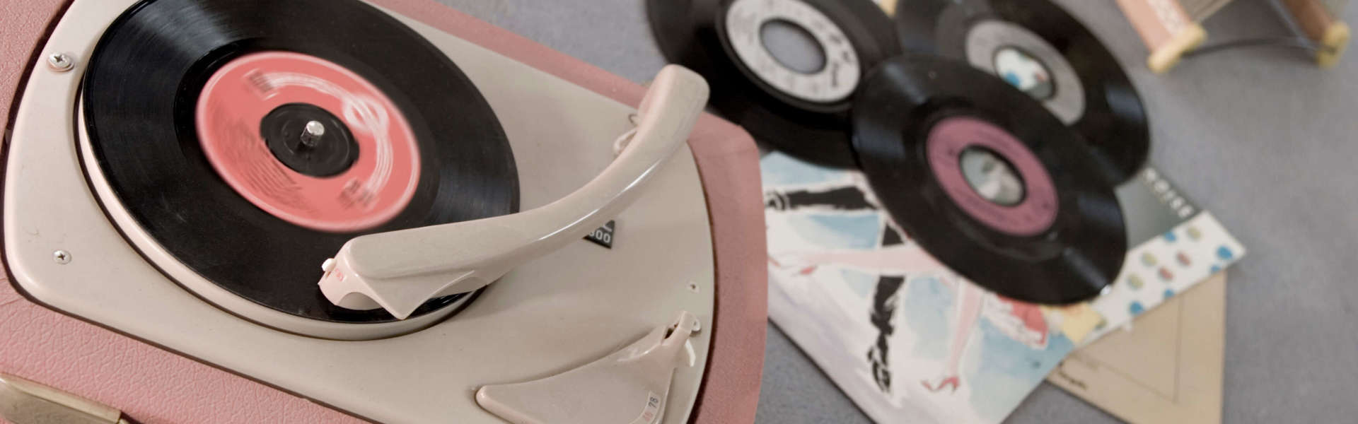 a pink vinyl record player playing a vinyl record with other discs laying next to it on the floor