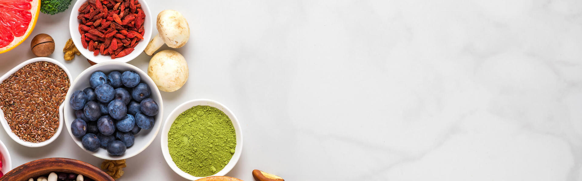 small bowls of fresh fruit vegetable and herbs on a white marble background