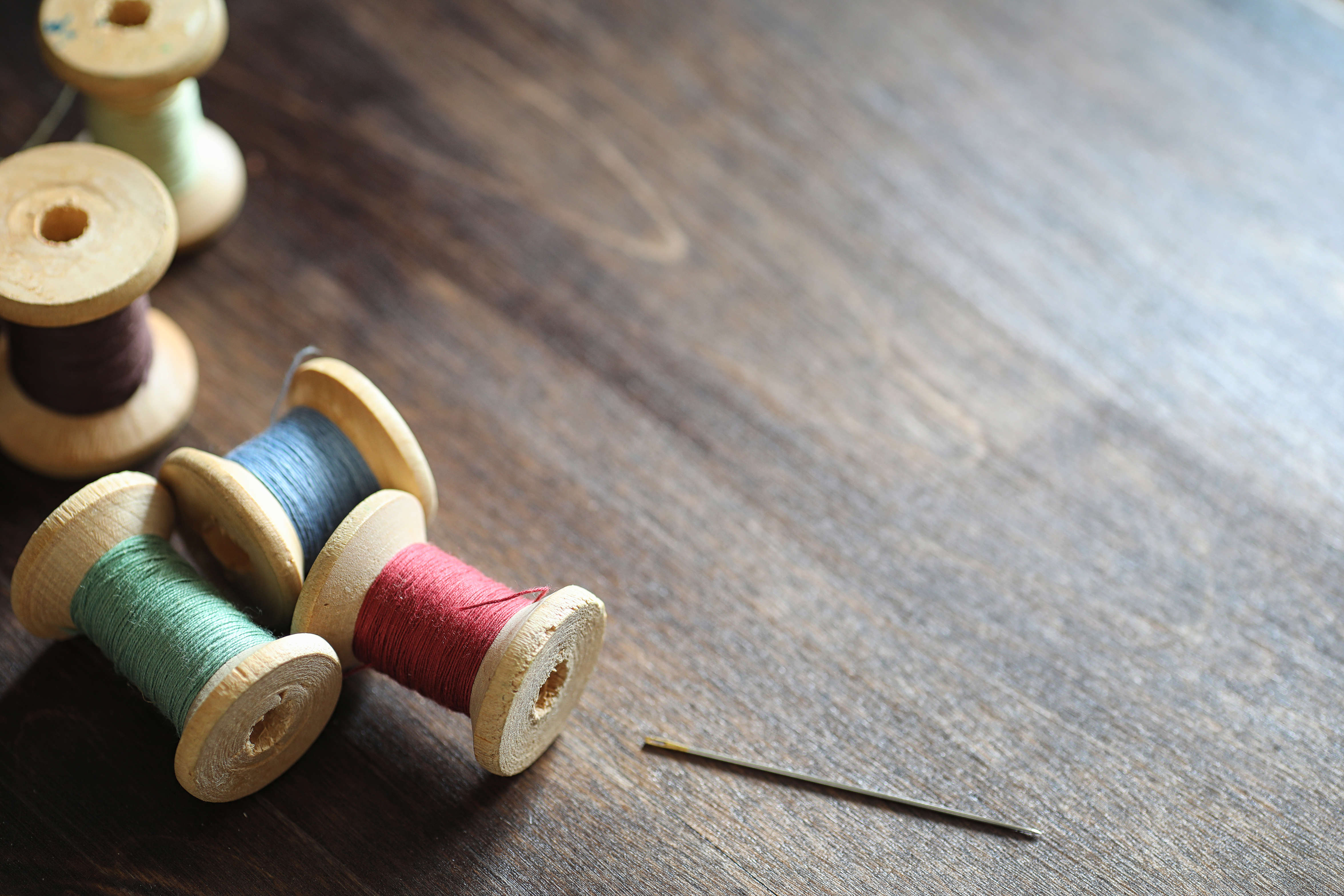 wooden bobbins with various coloured thread on a dark wooden table