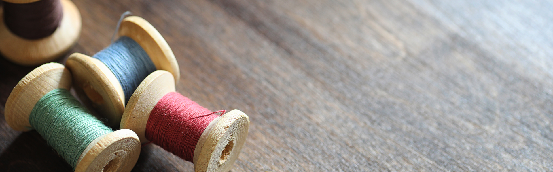 wooden bobbins with various coloured thread on a dark wooden table