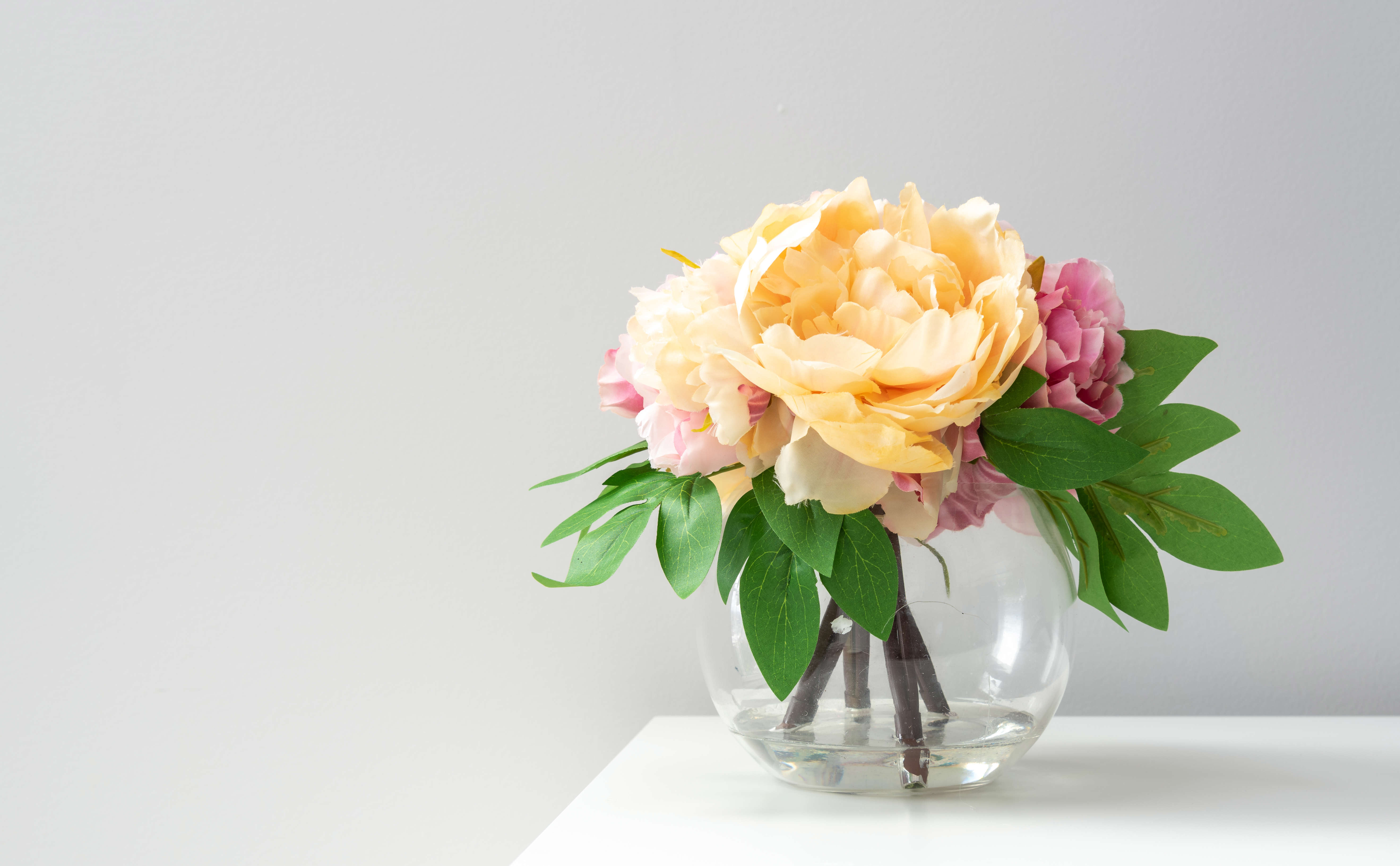 cut orange, pink and red peonies in a sphere shaped glass vase