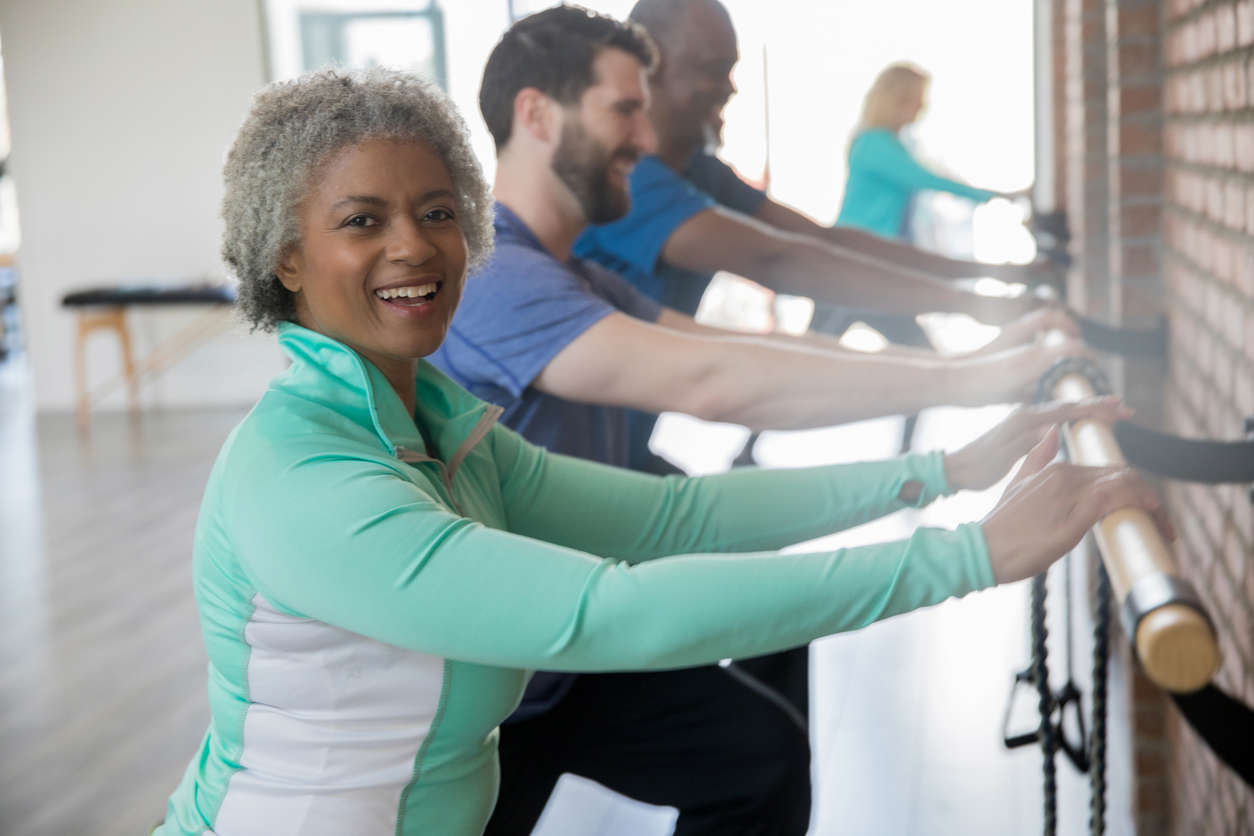 an older woman in a blue jacket stood at a ballet barre 