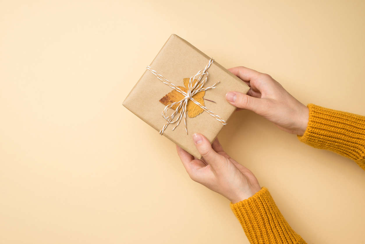 person holding a square parcel wrapped in brown paper, string and a leaf