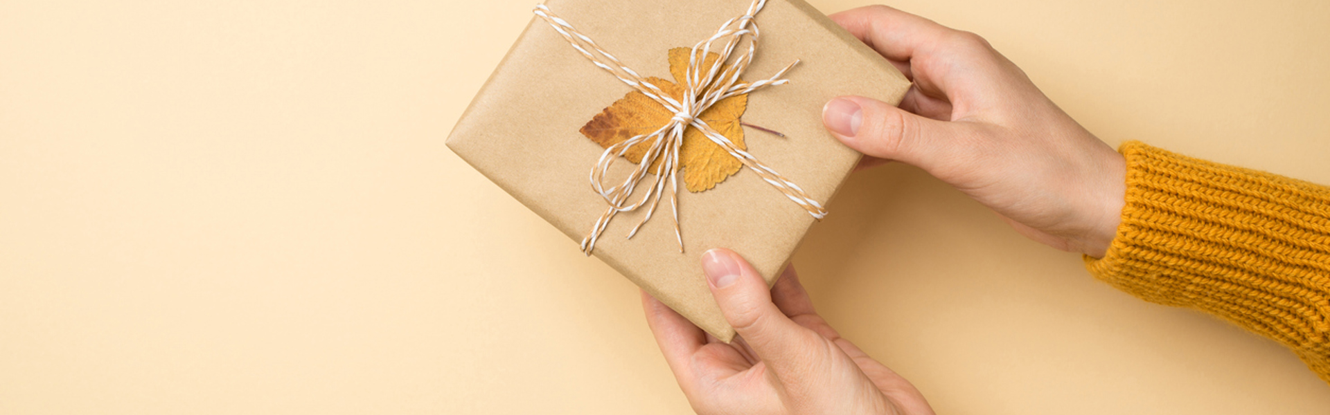 person holding a square parcel wrapped in brown paper, string and a leaf