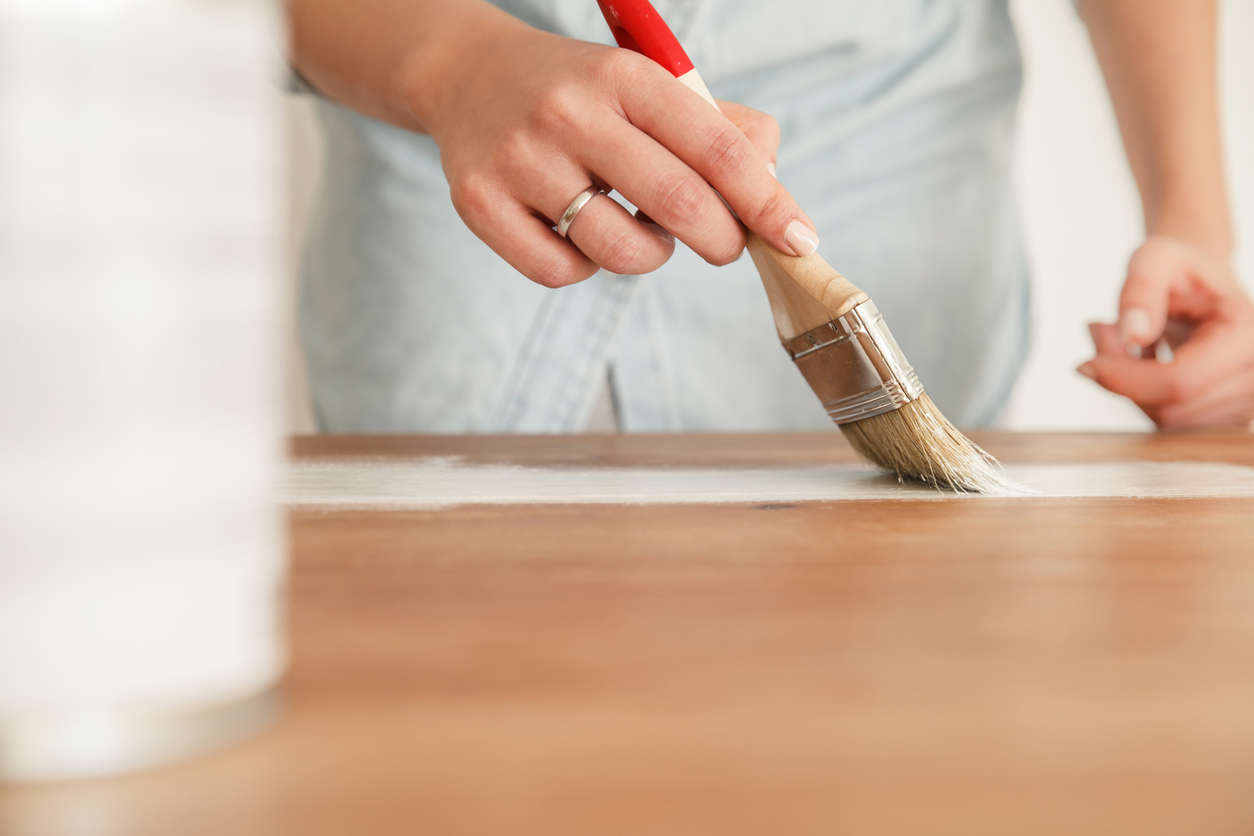 a close up of a person painting wood with a red paint brush