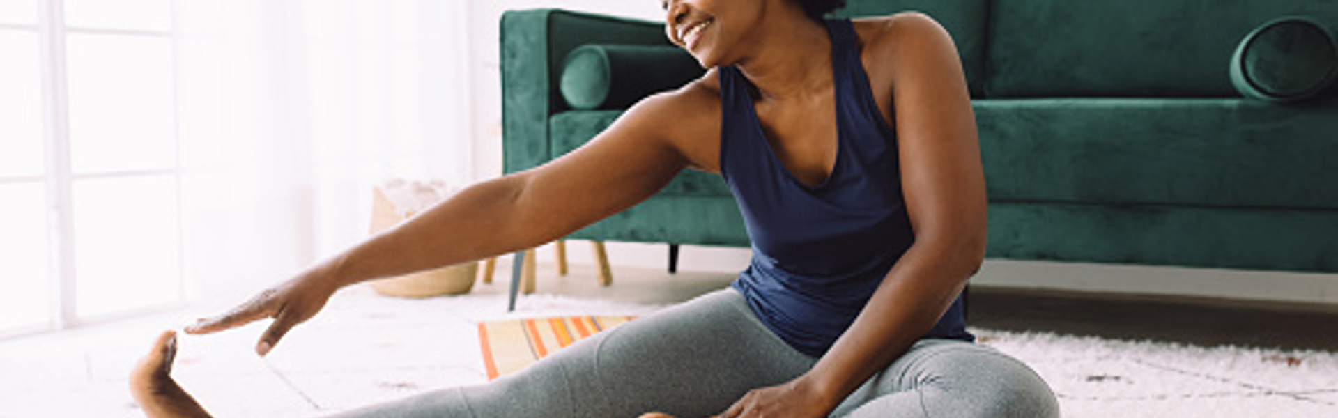 a woman sat on the living room floor on a yoga mat doing an online yoga class on her laptop