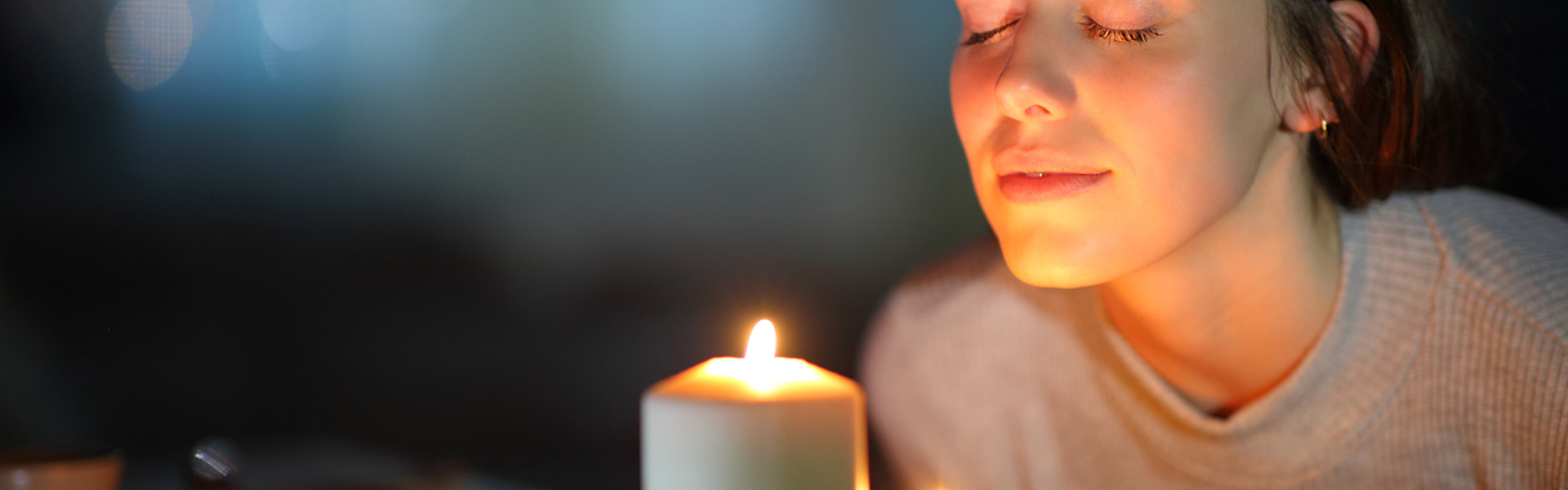 a woman leaning into candle light with her eyes closed meditating