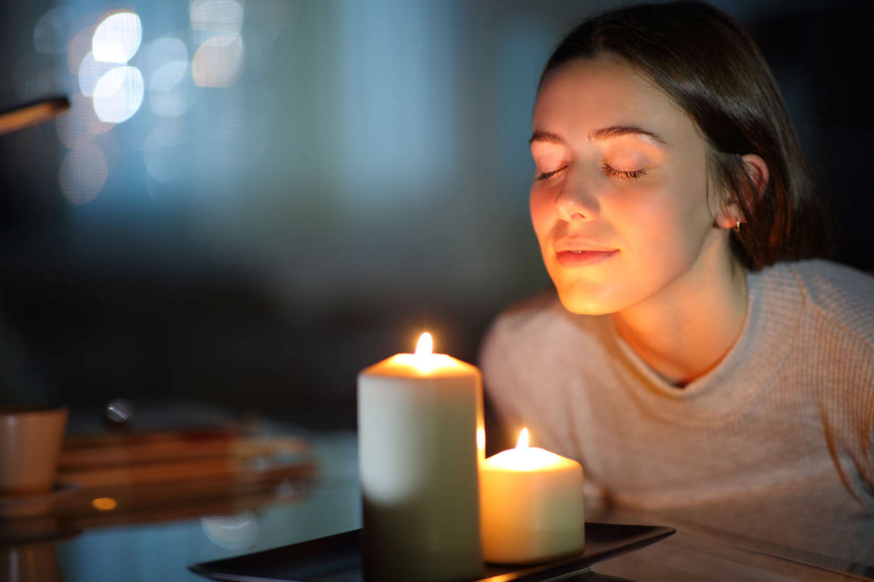 a woman leaning into candle light with her eyes closed meditating