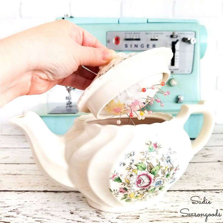 DIY Teapot Sewing Kit - a while teapot with a floral design on the front, with the lid being opened by a hand to reveal a pincushion inside the lid