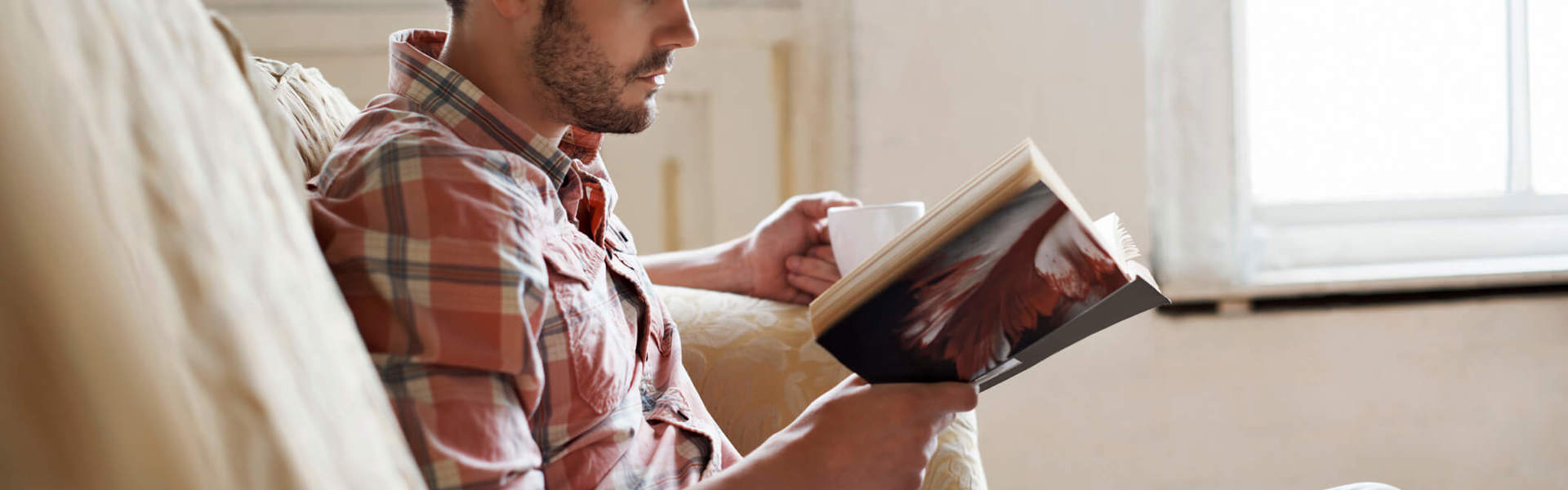 a man sat on the sofa with a cup of tea reading a book
