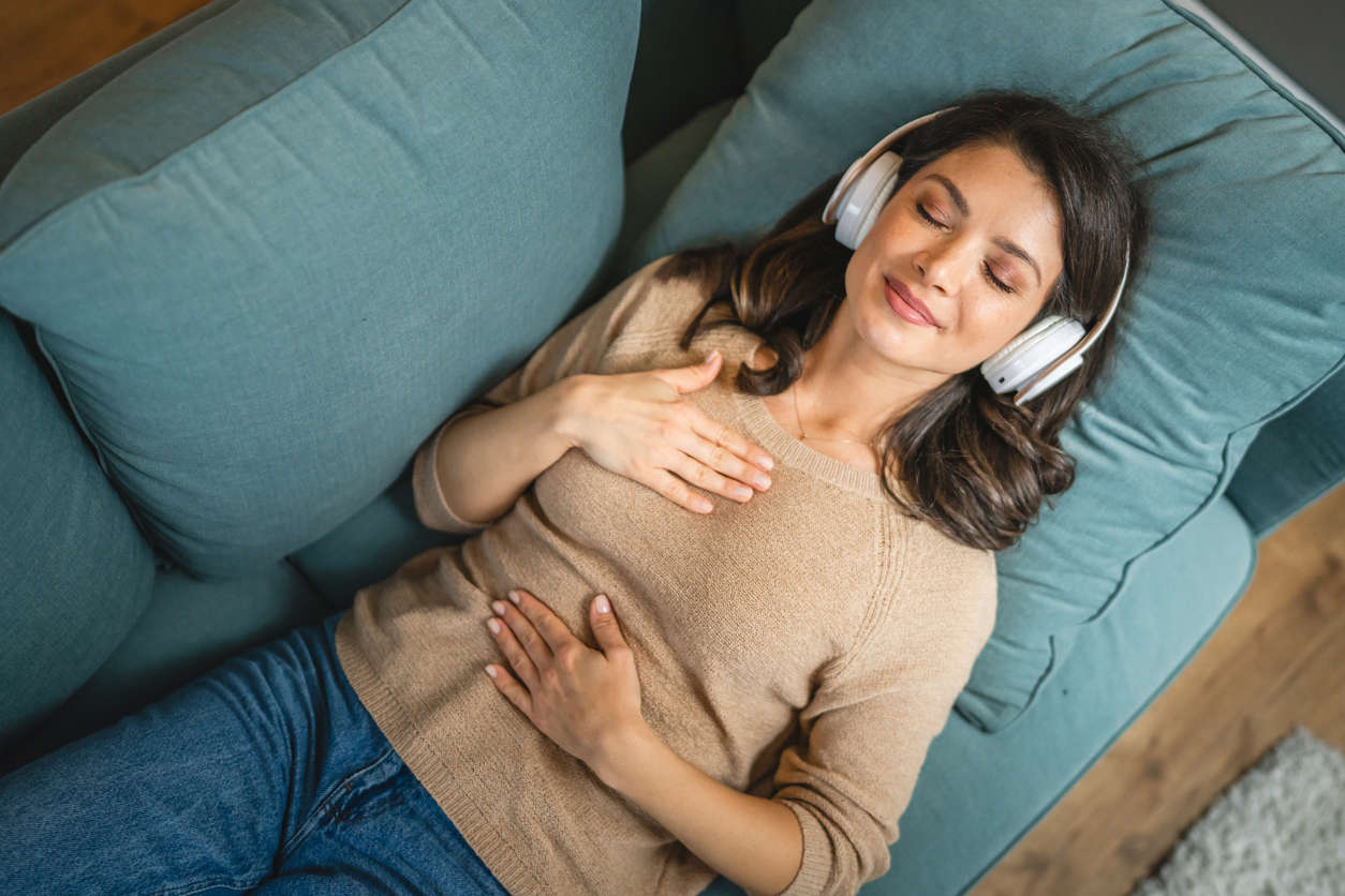 a woman wearing headphones laying on a blue sofa with her eyes closed practicing EFT Tapping