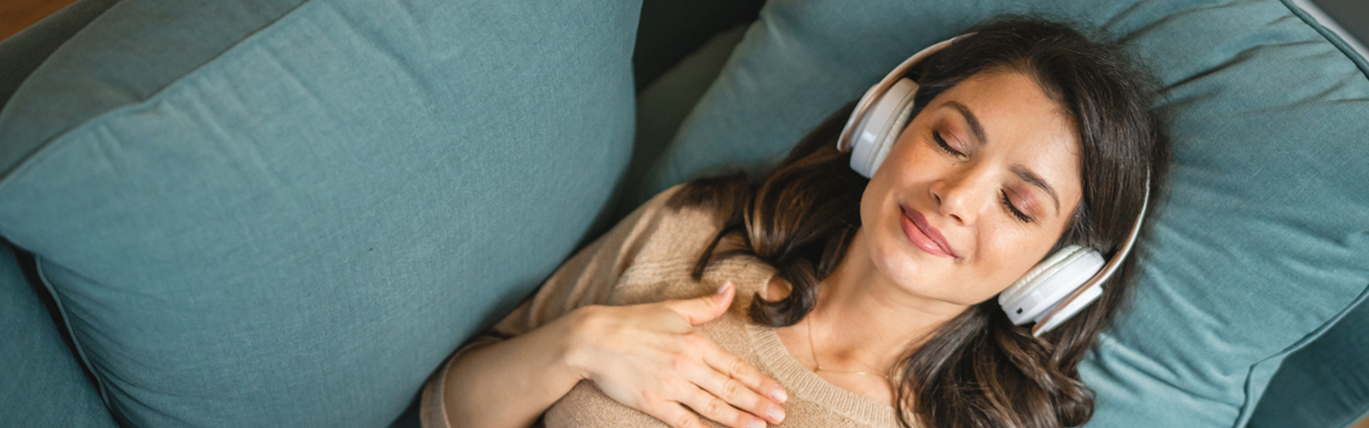 a woman wearing headphones laying on a blue sofa with her eyes closed practicing EFT Tapping
