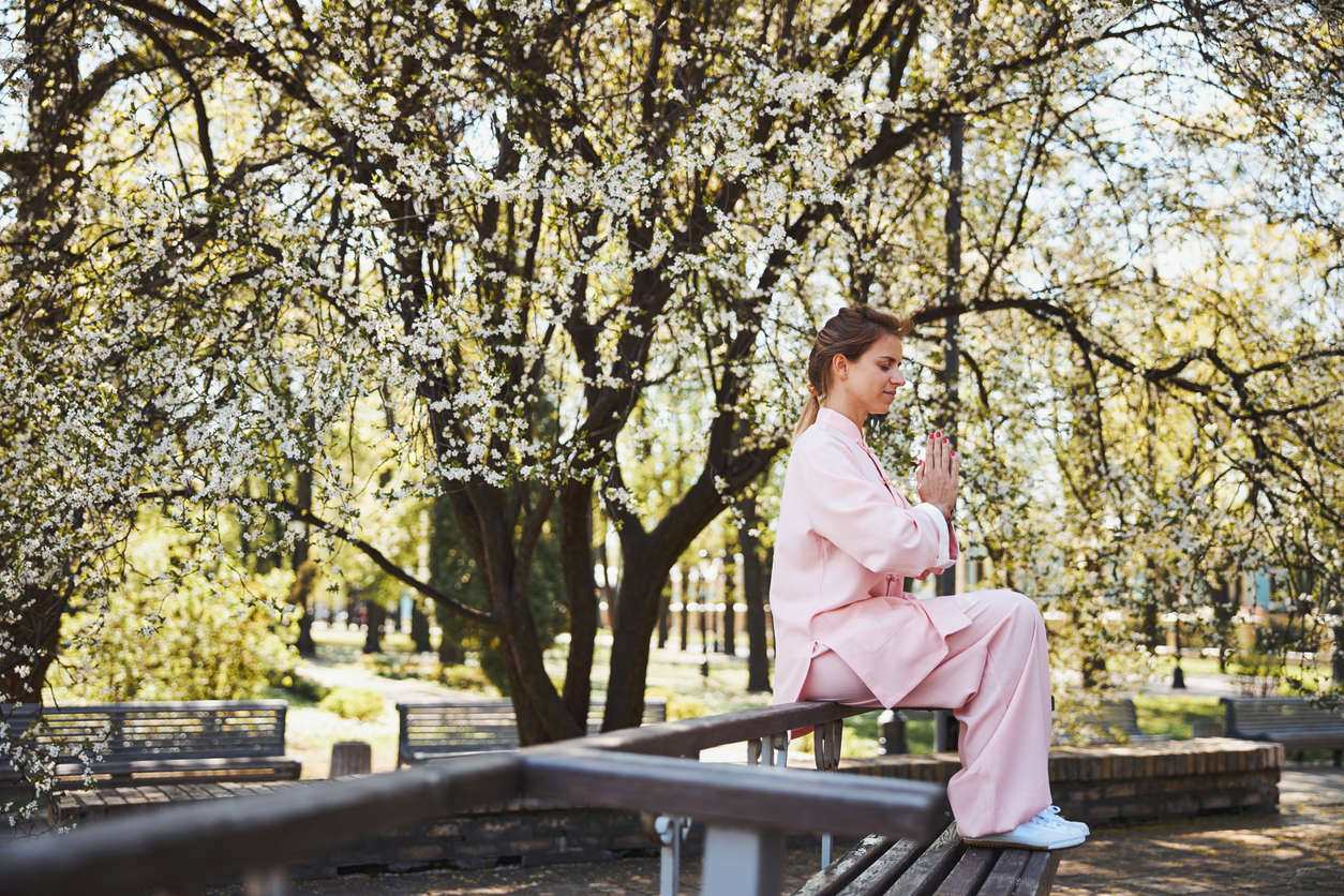 A woman wearing pink clothes sat on a bench outdoors practicing qi gong