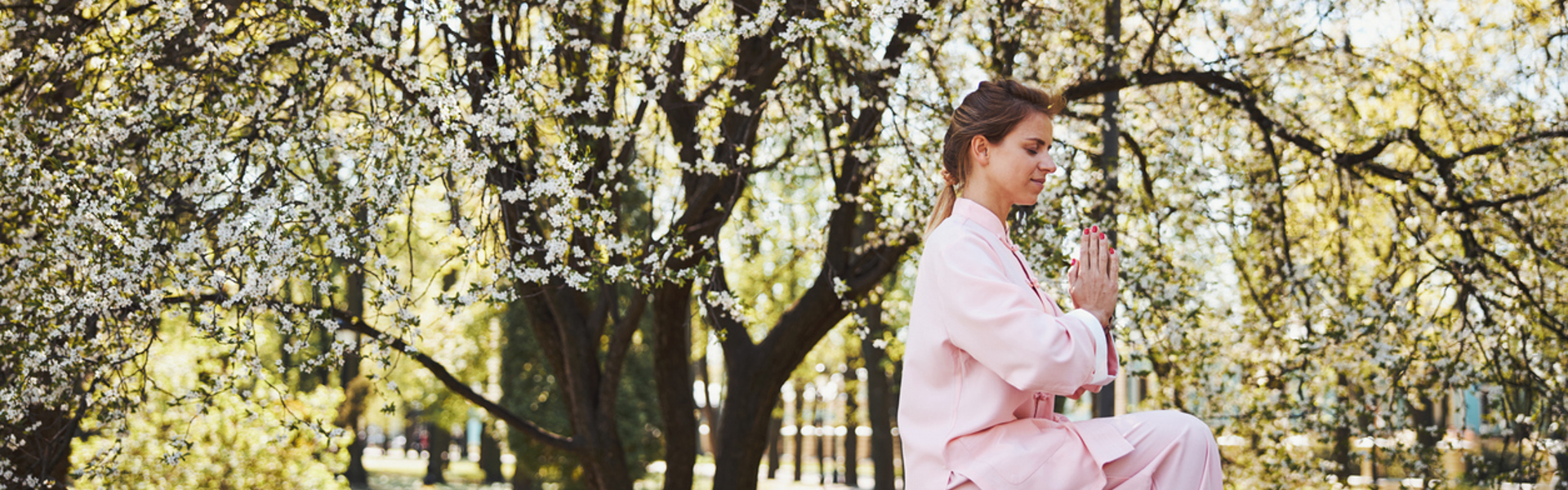 A woman wearing pink clothes sat on a bench outdoors practicing qi gong
