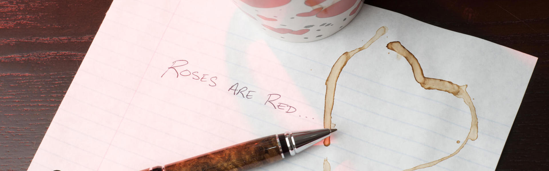 a mug of coffee resting on a valentine's day poem next to a pen and heart shaped coffee mark