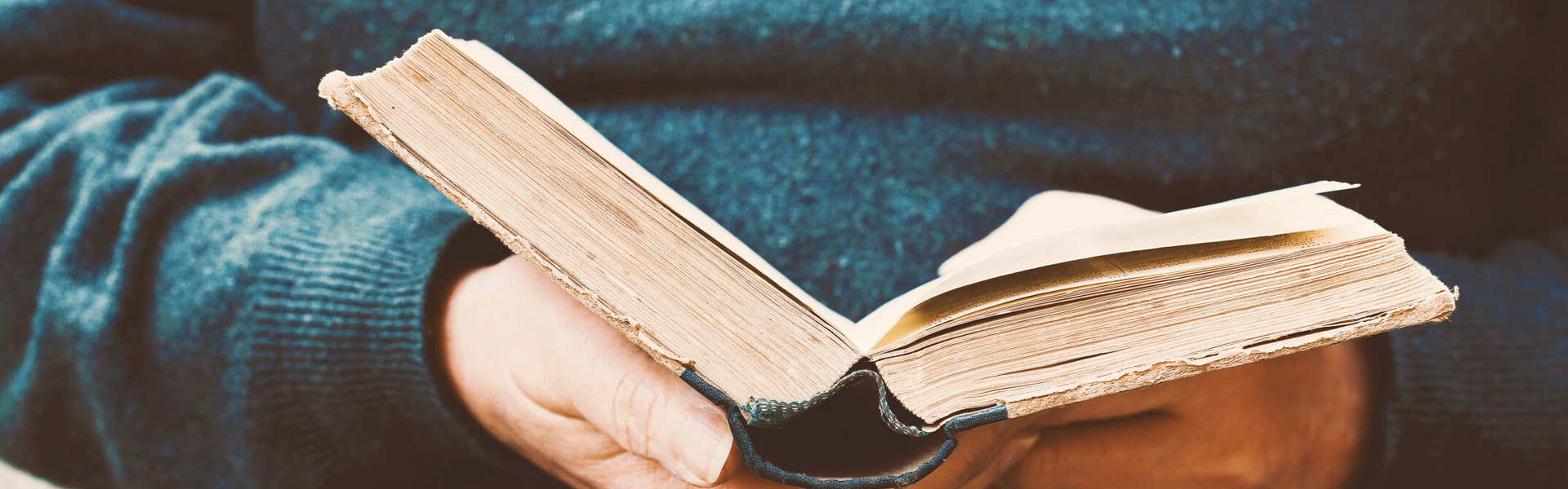 a close up of someone wearing a blue jumper holding a book open and reading it