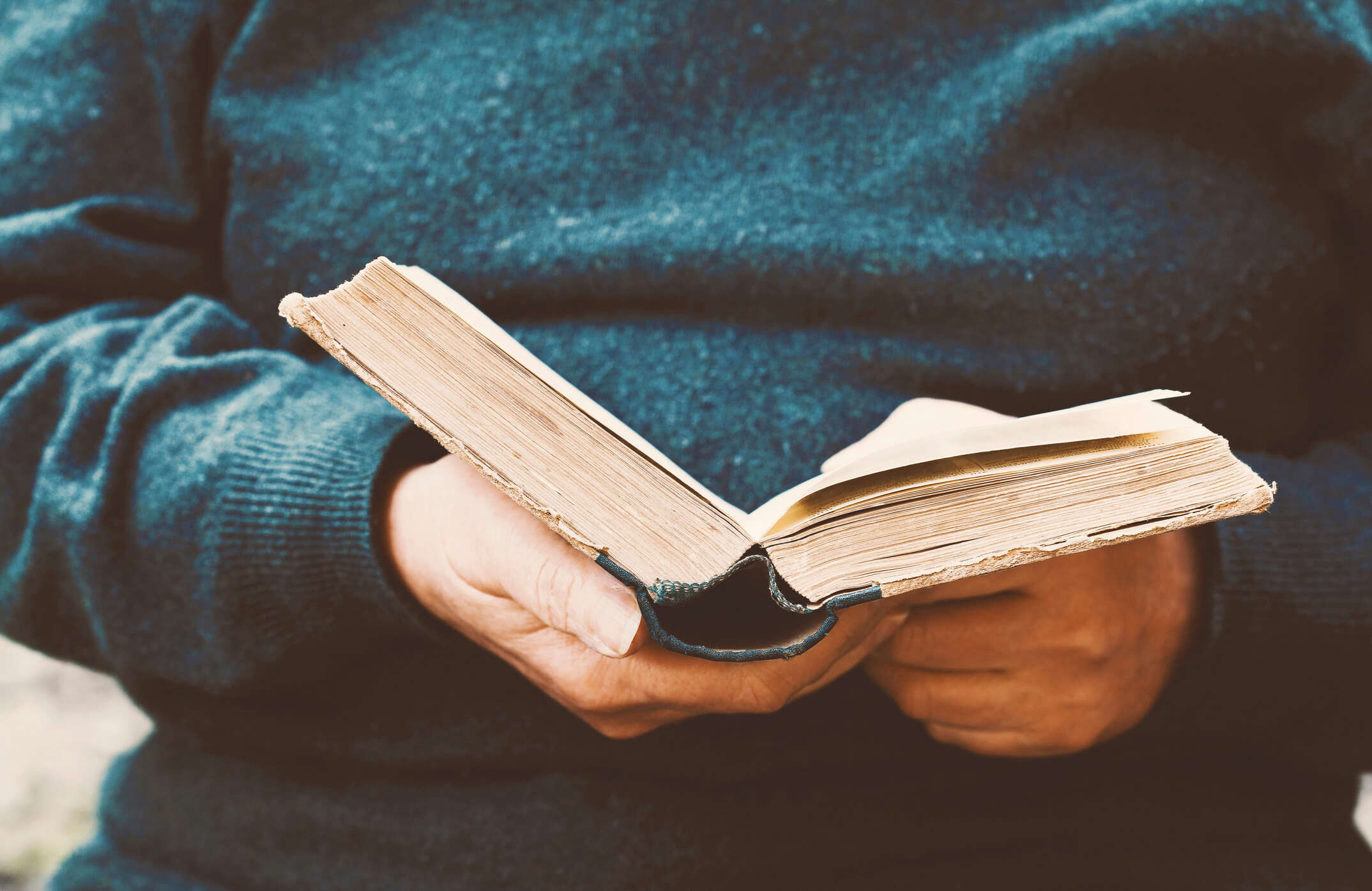 a close up of someone wearing a blue jumper holding a book open and reading it