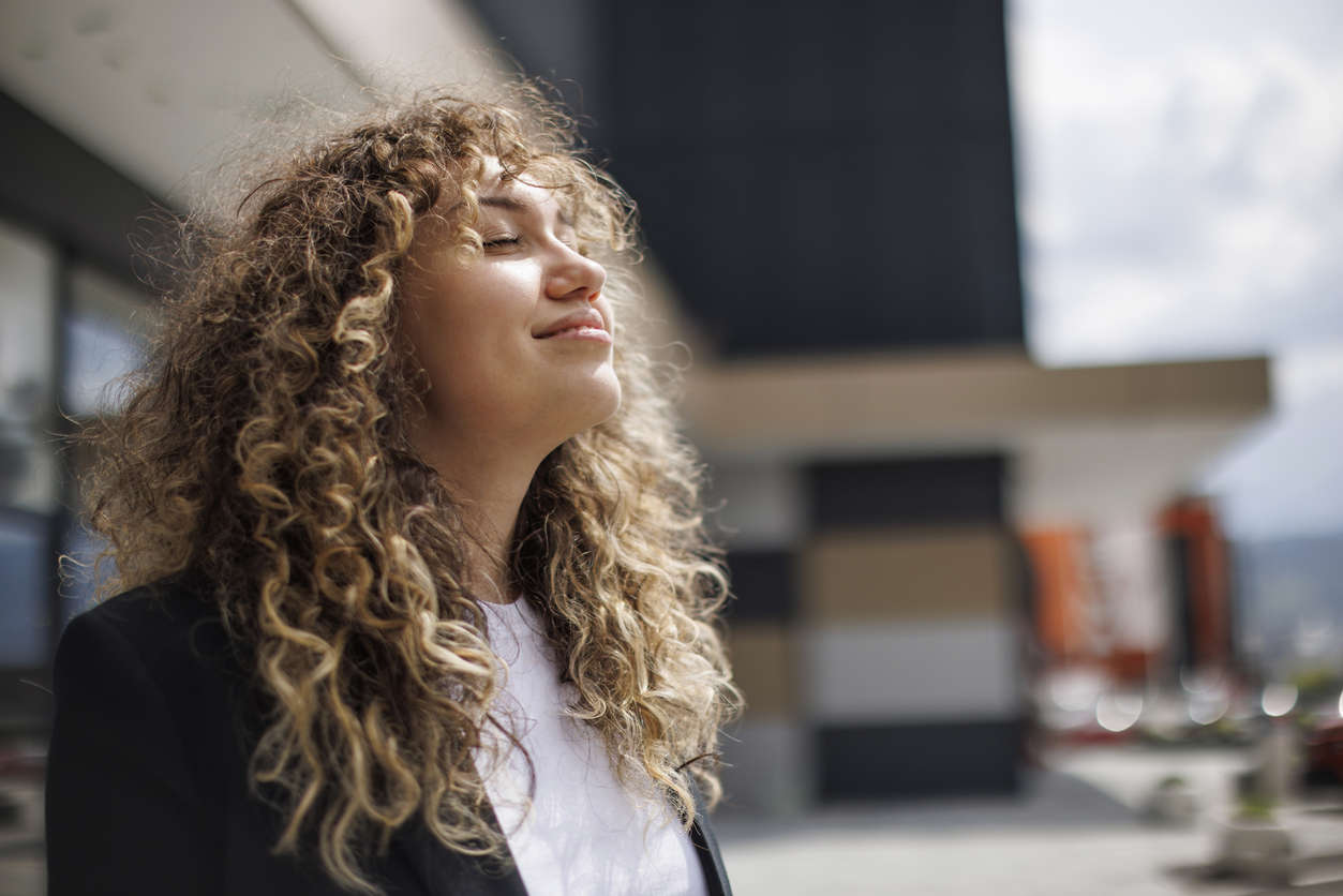 a woman stood outside with her eyes closed smiling in the sunshine