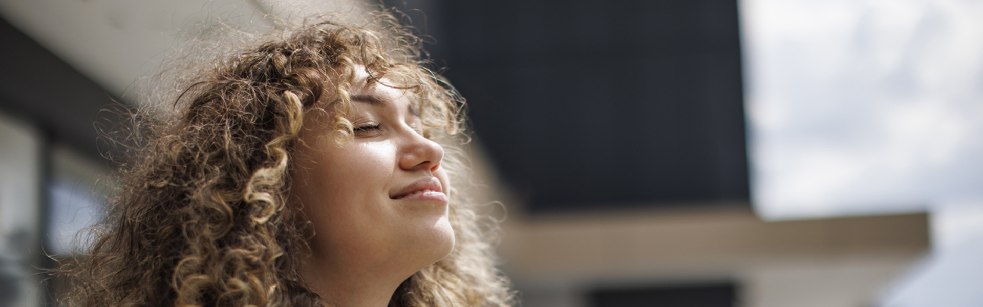 a woman stood outside with her eyes closed smiling in the sunshine