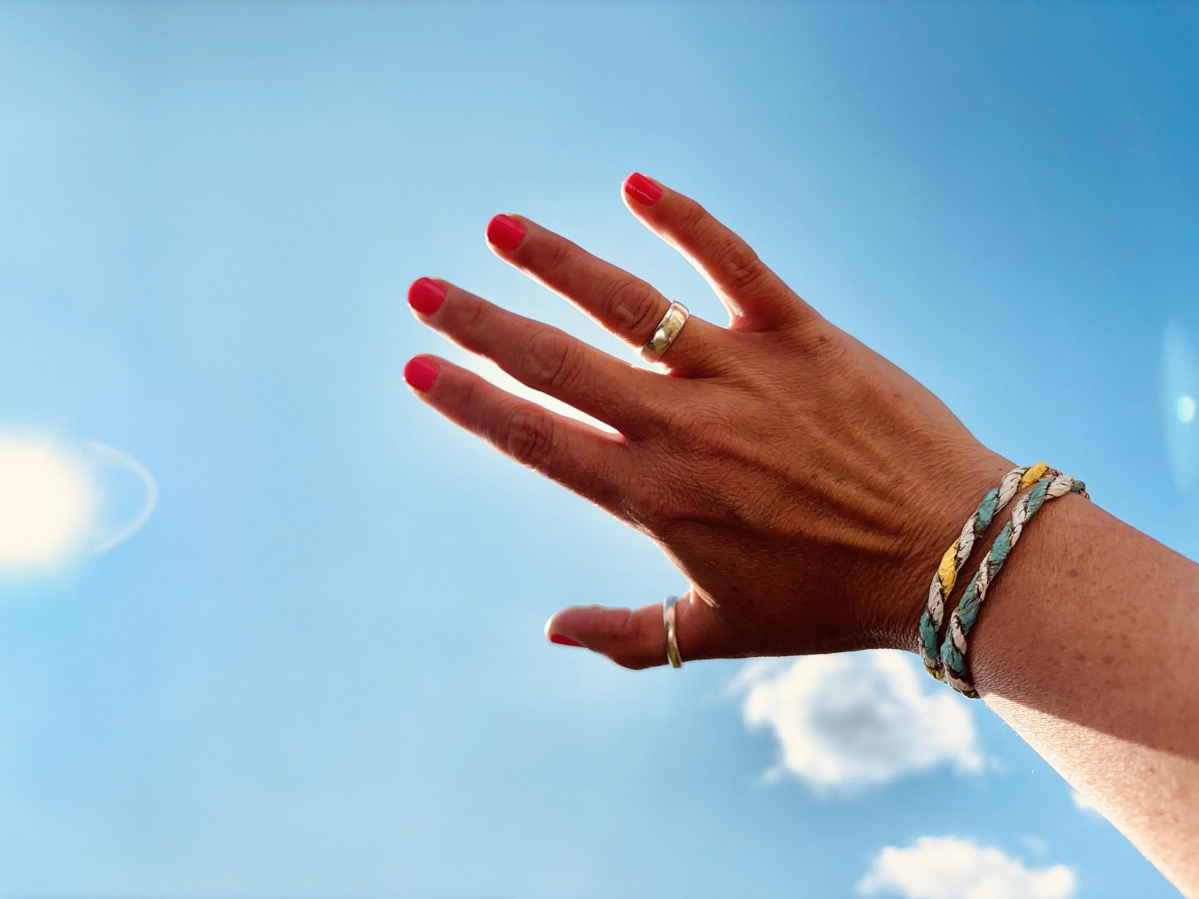 Main Image: Person wearing friendship bracelets using paper bags, holding their hand up to the blue sky on a sunny day.