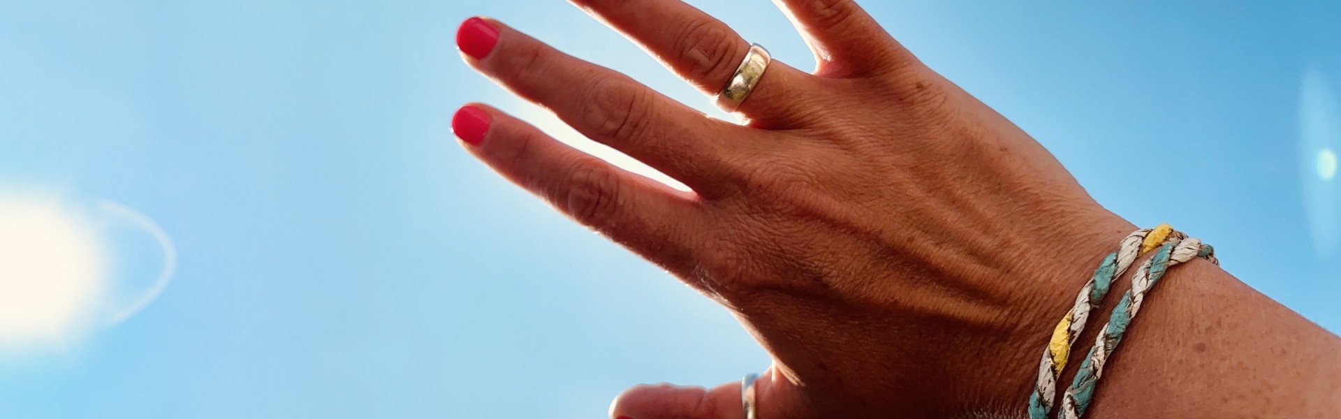Main Image: Person wearing friendship bracelets using paper bags, holding their hand up to the blue sky on a sunny day.