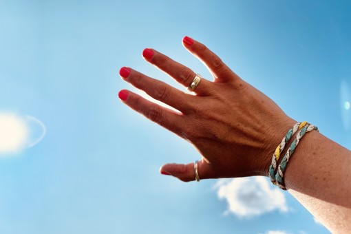 Main Image: Person wearing friendship bracelets using paper bags, holding their hand up to the blue sky on a sunny day.
