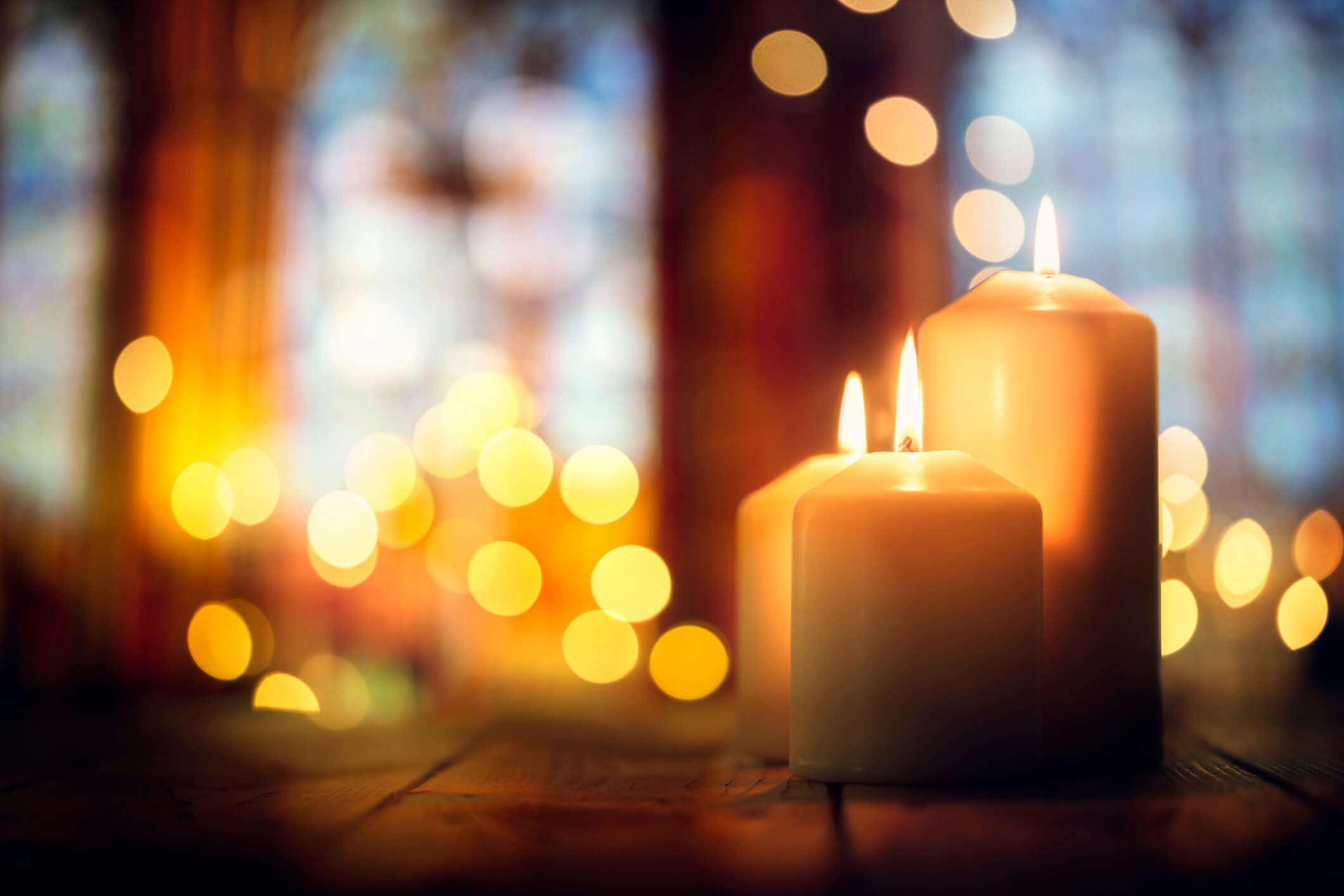 two pillar candles lit  in the foreground with candle lighting glowing in the background