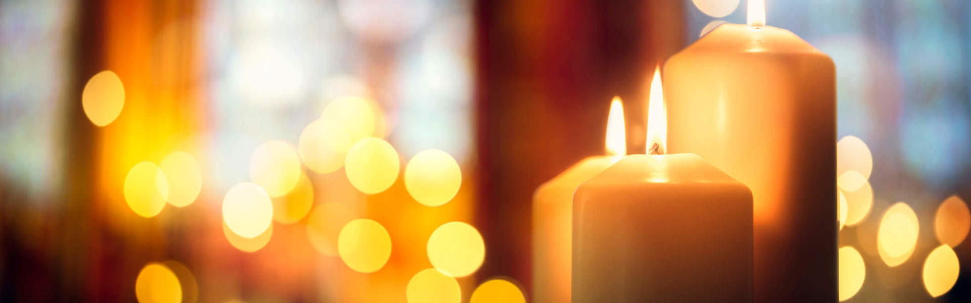 two pillar candles lit  in the foreground with candle lighting glowing in the background