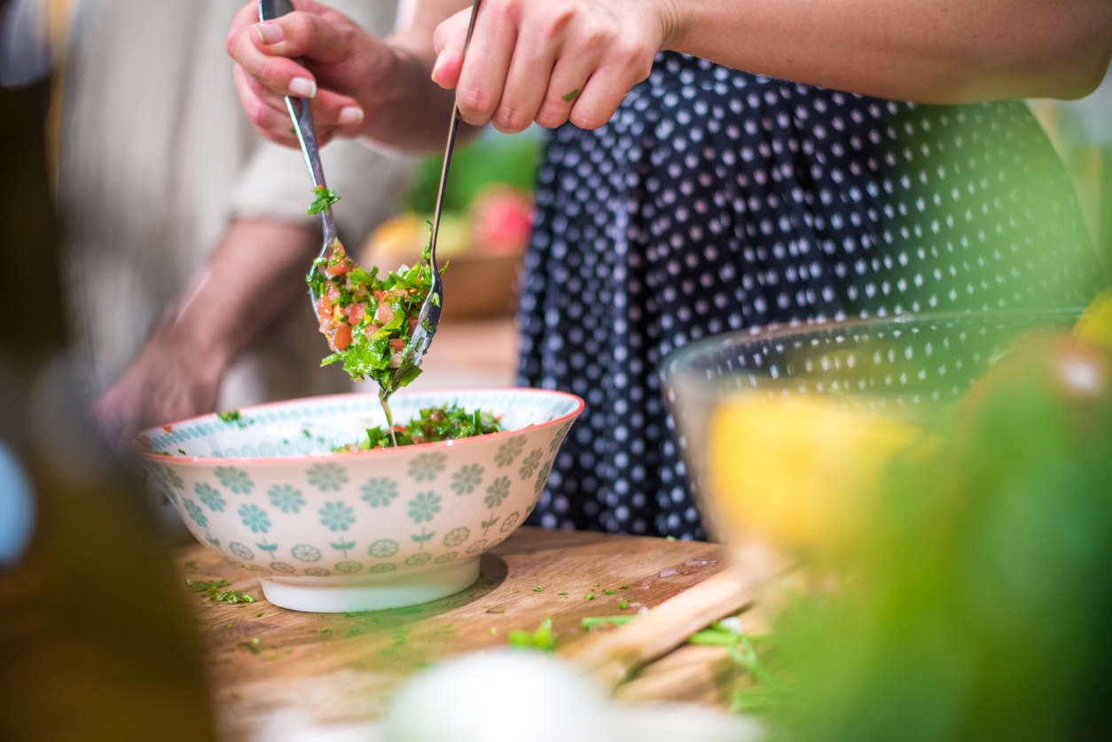 a woman tossing a fresh chopped tomato and greens salad wearing a blue and white polka dot dress