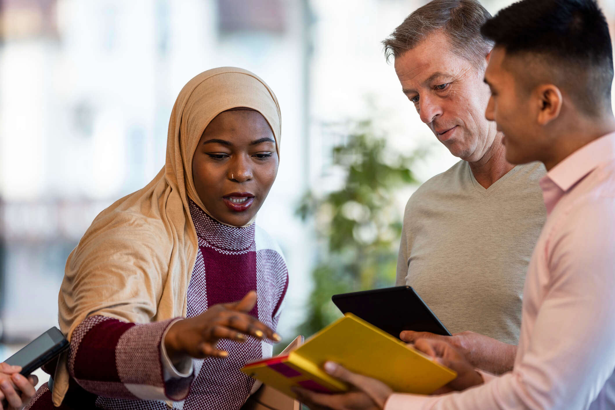 a woman explaining something to two men using a tablet