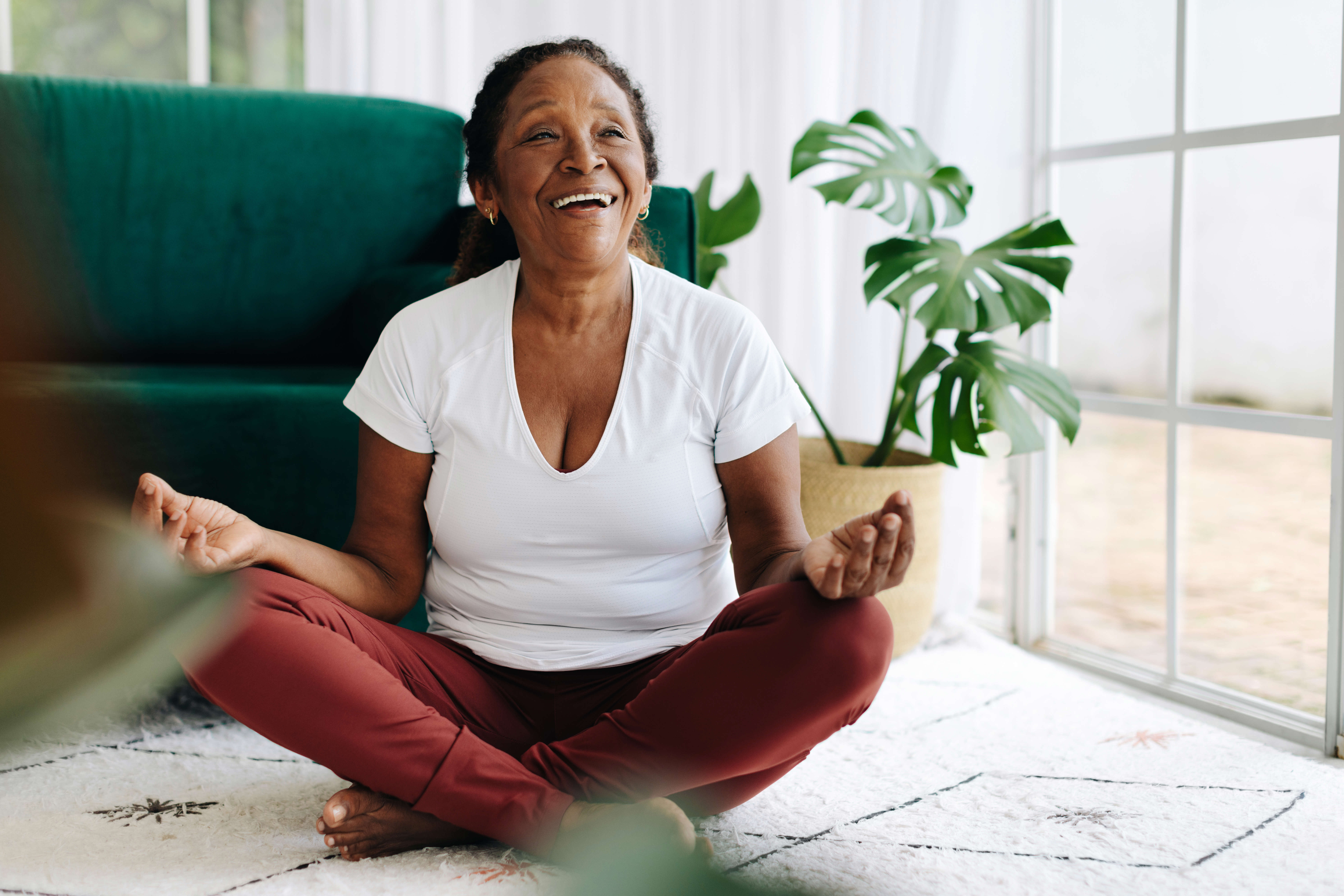 Main image: an older woman, sat in lotus position, laughing during a laughter yoga class.