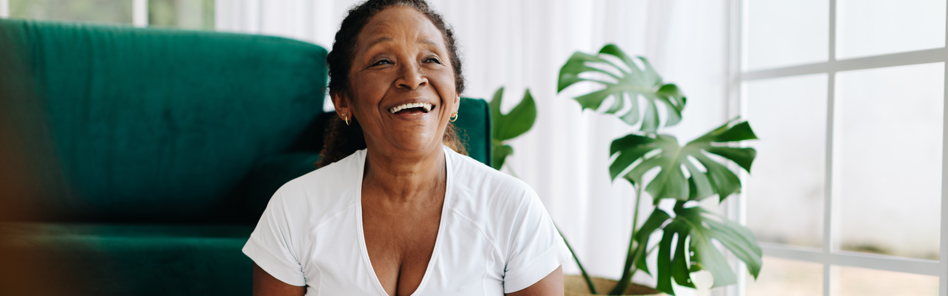 Main image: an older woman, sat in lotus position, laughing during a laughter yoga class.