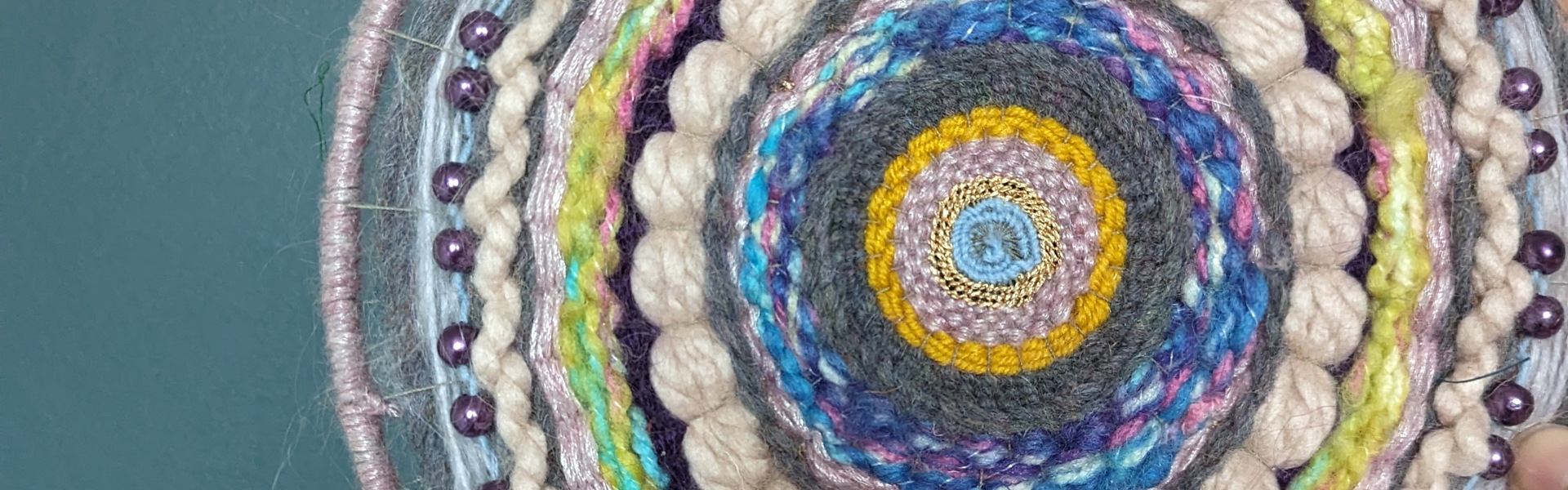 multi-coloured weaved wall hanging in a variety of string and thread material against a teal blue background