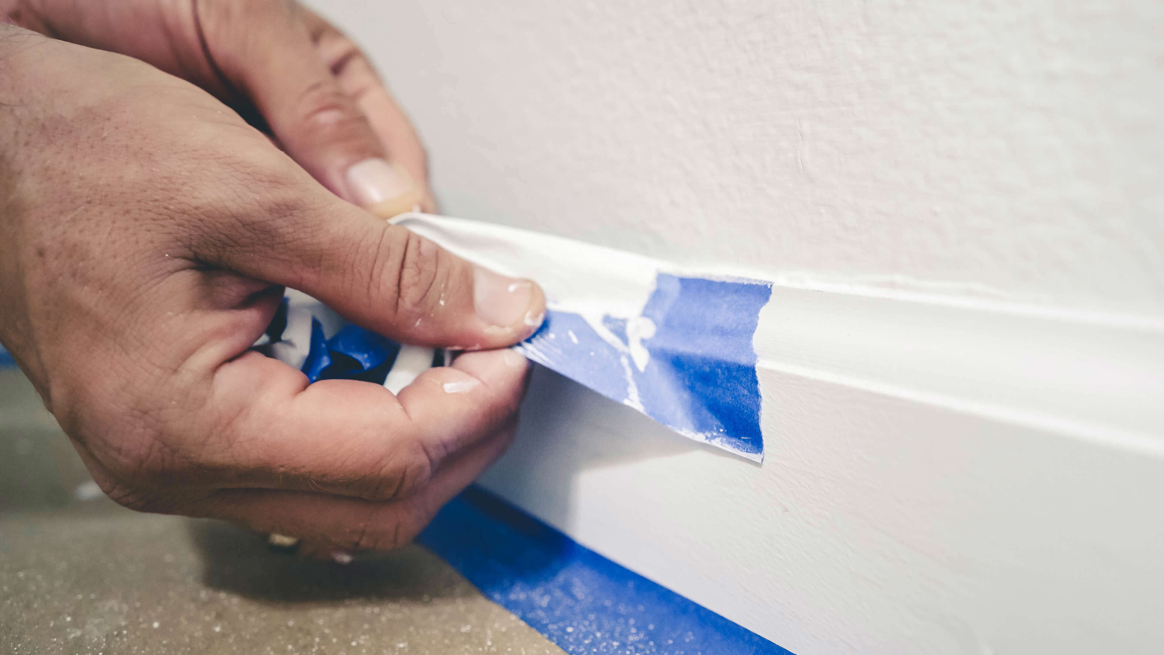 a close up of someone peeling blue masking tape of a white painted wall