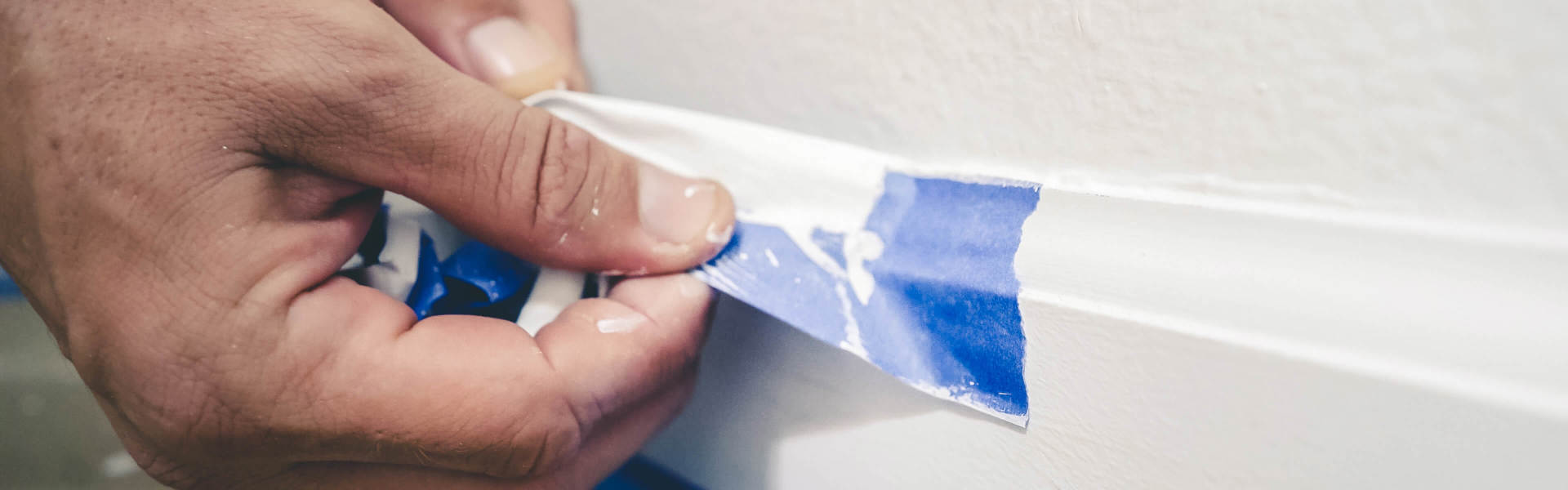 a close up of someone peeling blue masking tape of a white painted wall