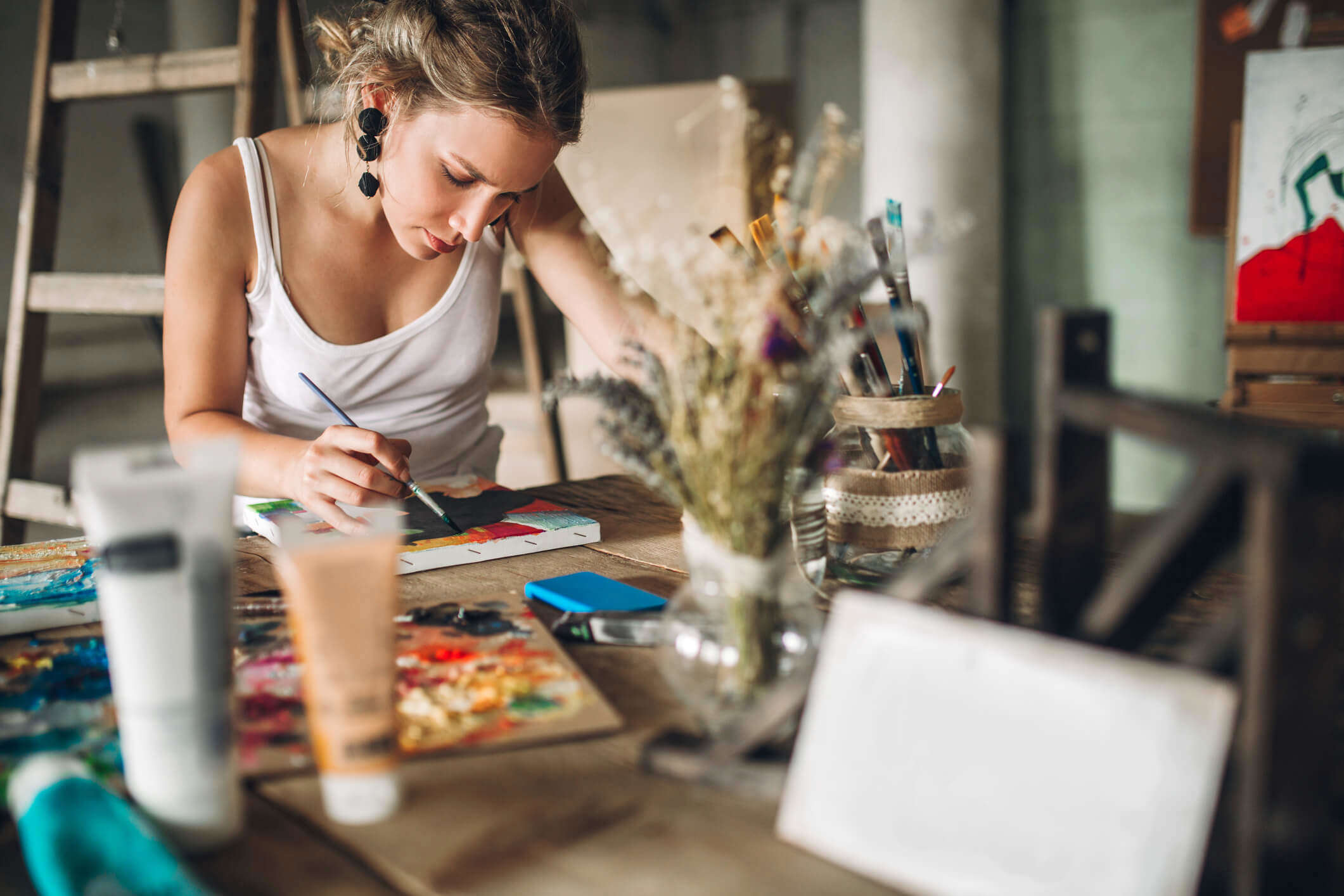 a woman sat a table painting in an art studio