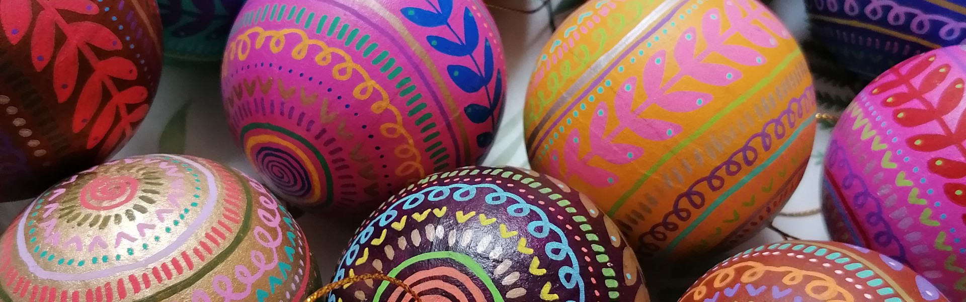 decorative baubles is a variety of colours with hand painted patterns painted onto them with gold string attached to each of them