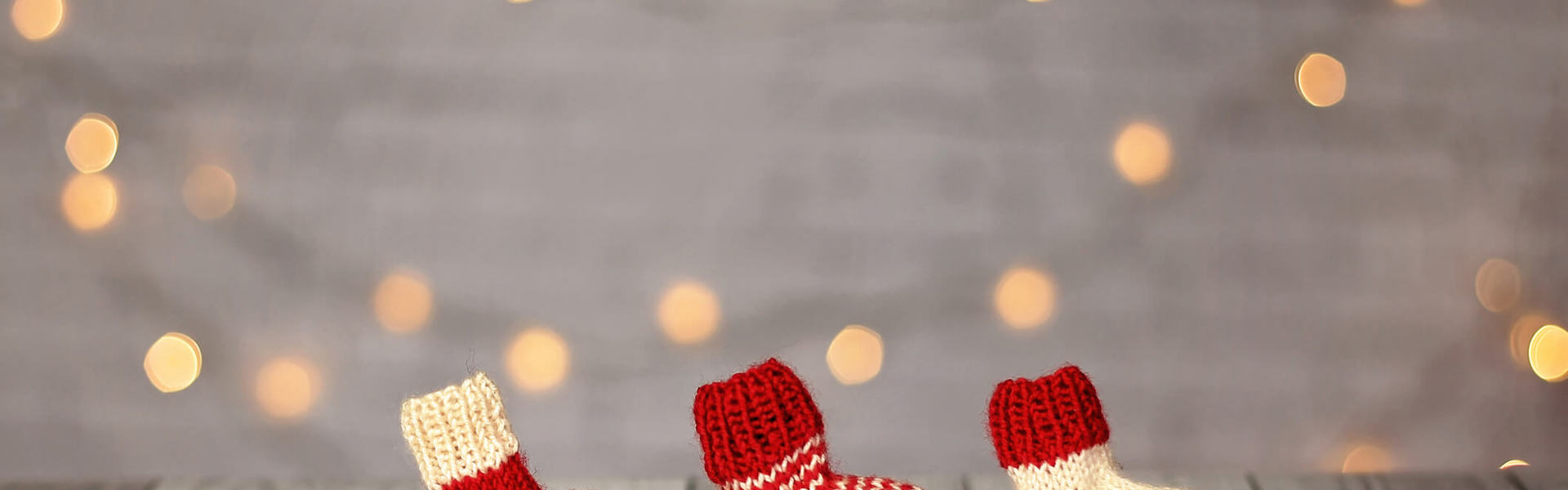 three red and white mini crochet Christmas stockings lined up on a white background surrounded by Christmas fairy lights