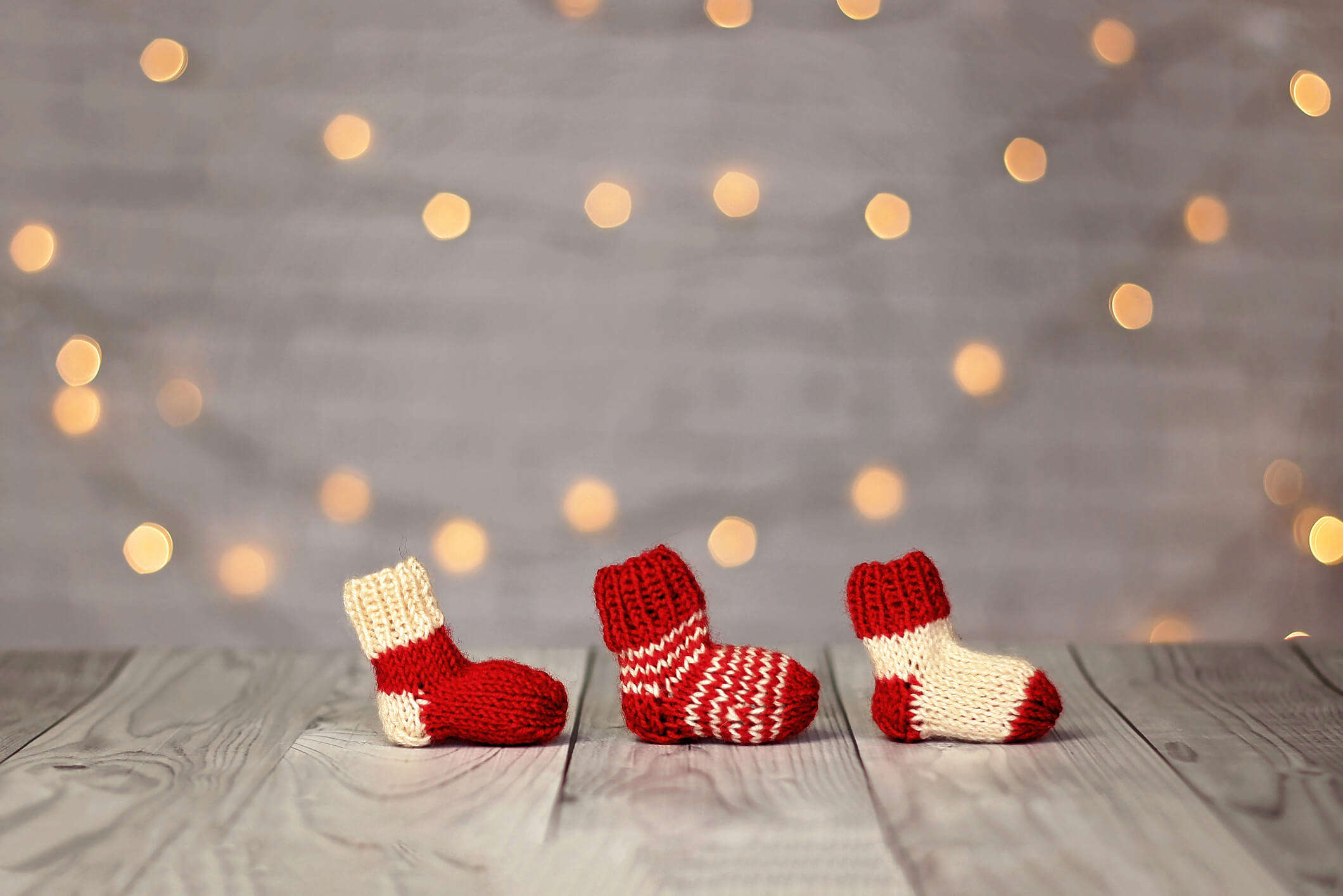 three red and white mini crochet Christmas stockings lined up on a white background surrounded by Christmas fairy lights