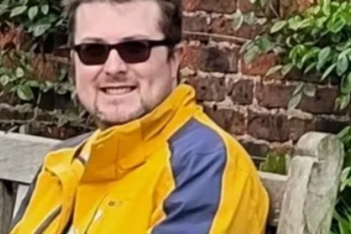 Photo of Chris Jesson, Groovy Gardening UK, smiling sat on a bench wearing sunglasses and a yellow jacket.