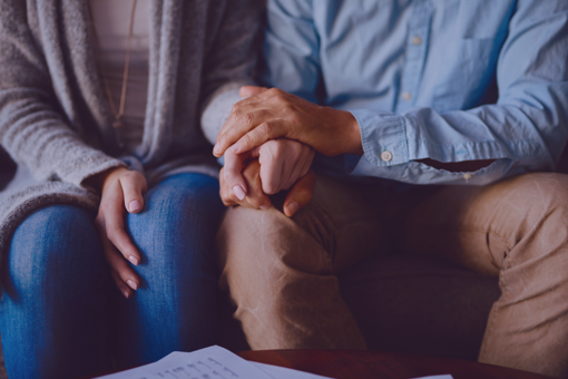 Main Image: Two people sat on a sofa, comforting each other holding hands, the image cuts off at their shoulders.