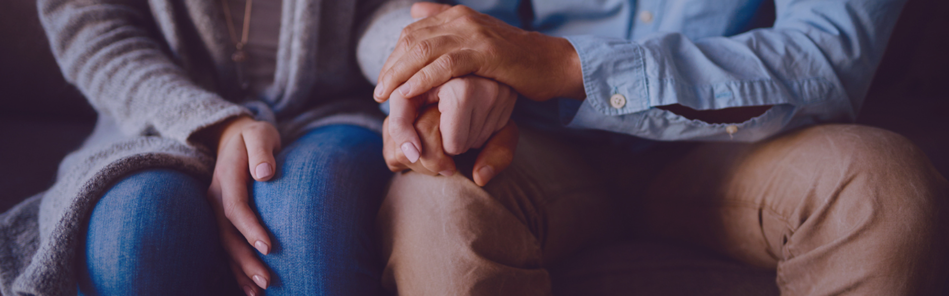 Main Image: Two people sat on a sofa, comforting each other holding hands, the image cuts off at their shoulders.