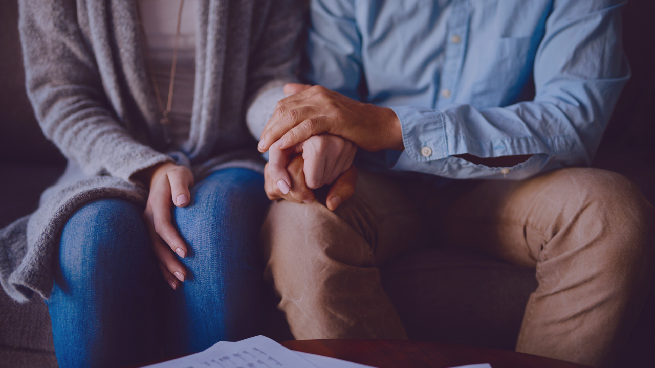 Main Image: Two people sat on a sofa, comforting each other holding hands, the image cuts off at their shoulders.