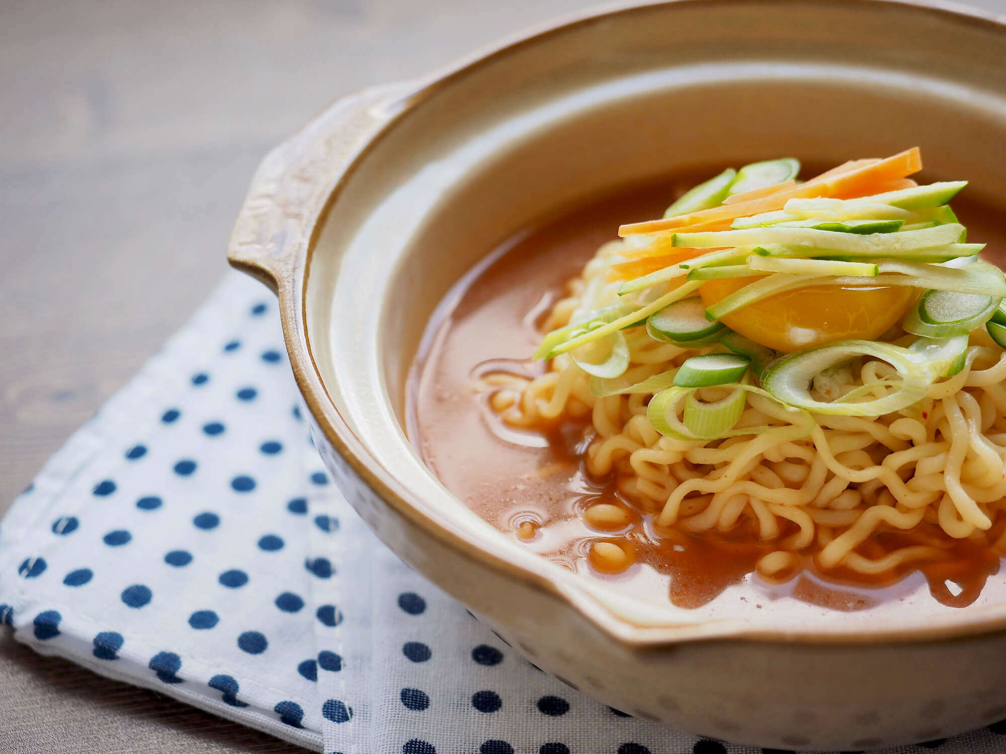 a close up of fresh noodle soup in a bowl on a polka dot napkin