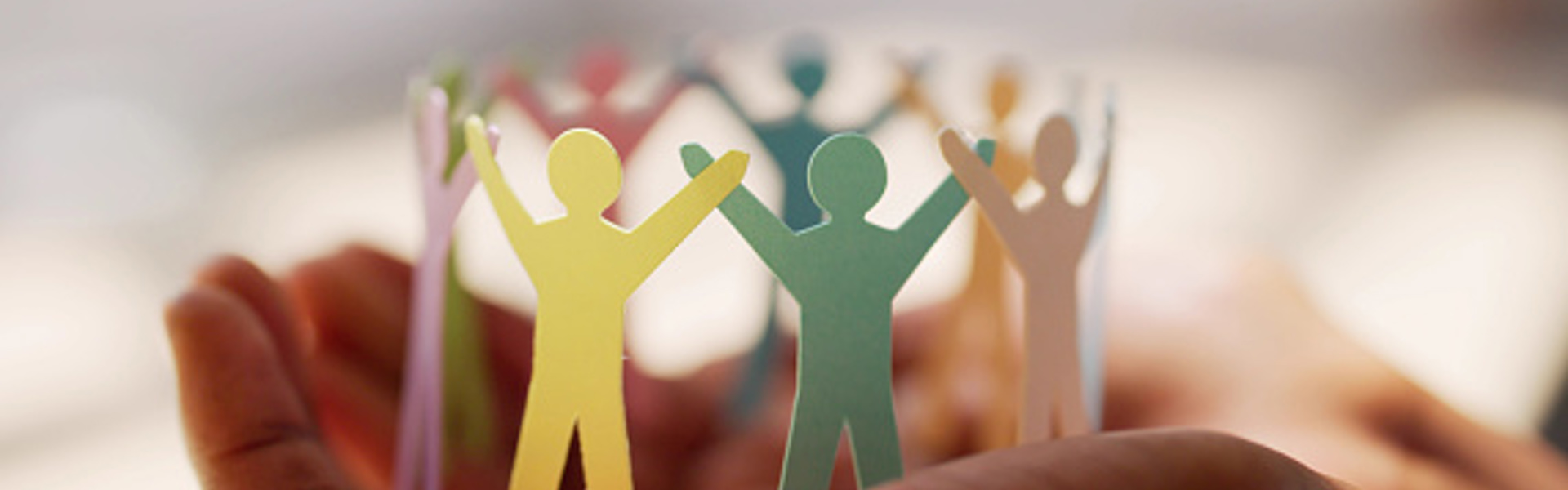 a ring of multicoloured paper people resting in the palm of a pair of hands