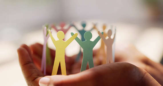 a ring of multicoloured paper people resting in the palm of a pair of hands