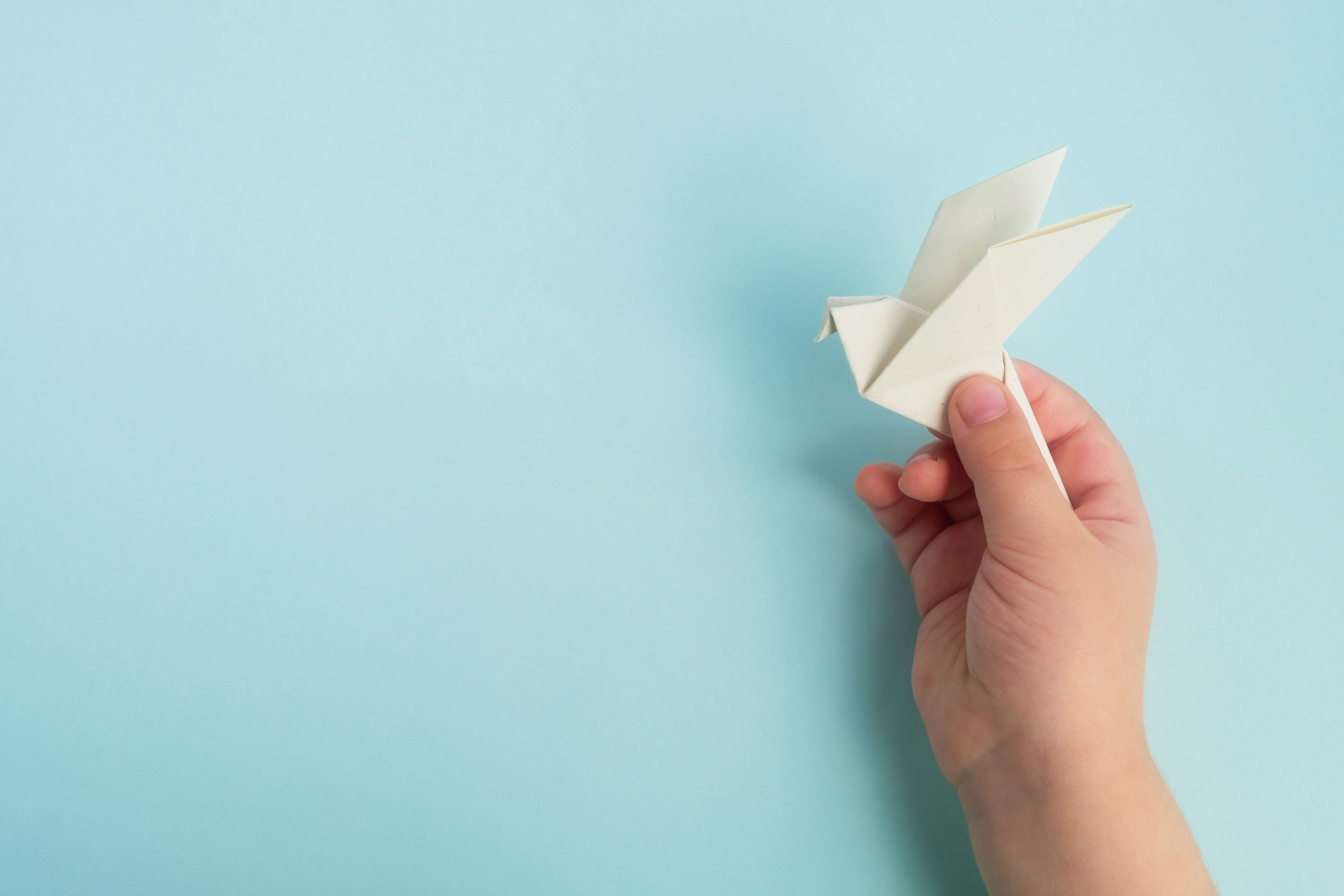 a child's hand holding a white paper origami bird on a blue background