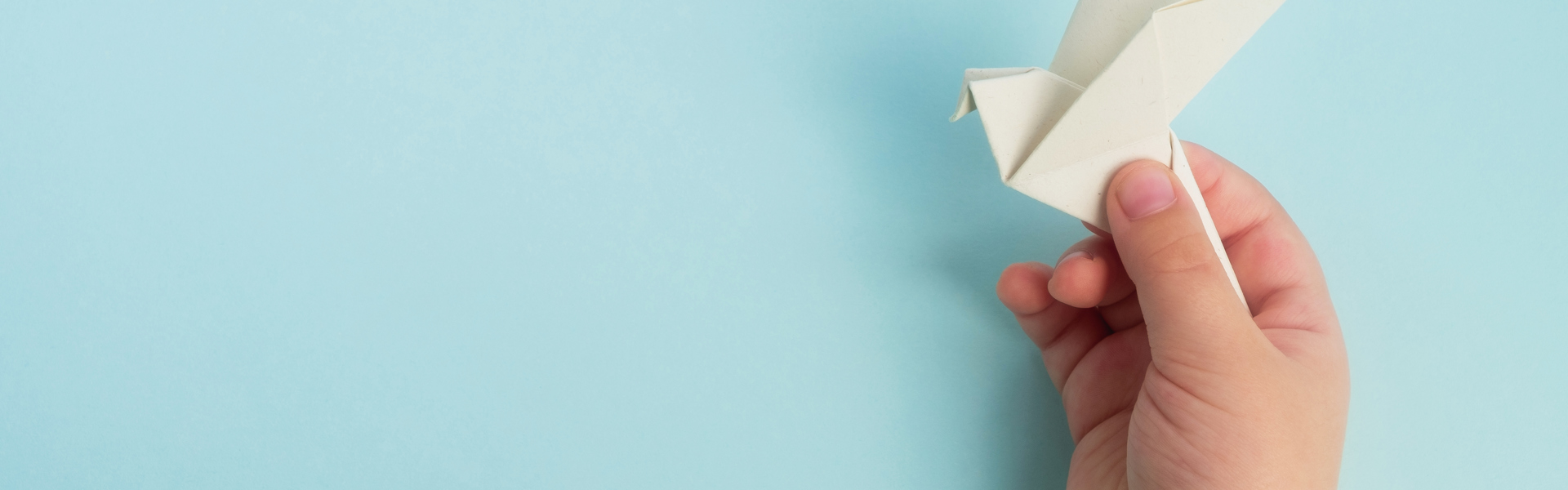 a child's hand holding a white paper origami bird on a blue background