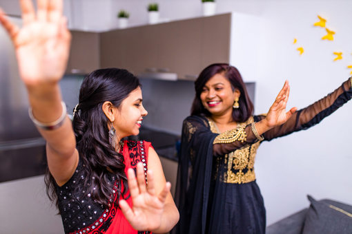 two women in black and gold and red sarees dancing in the kitchen